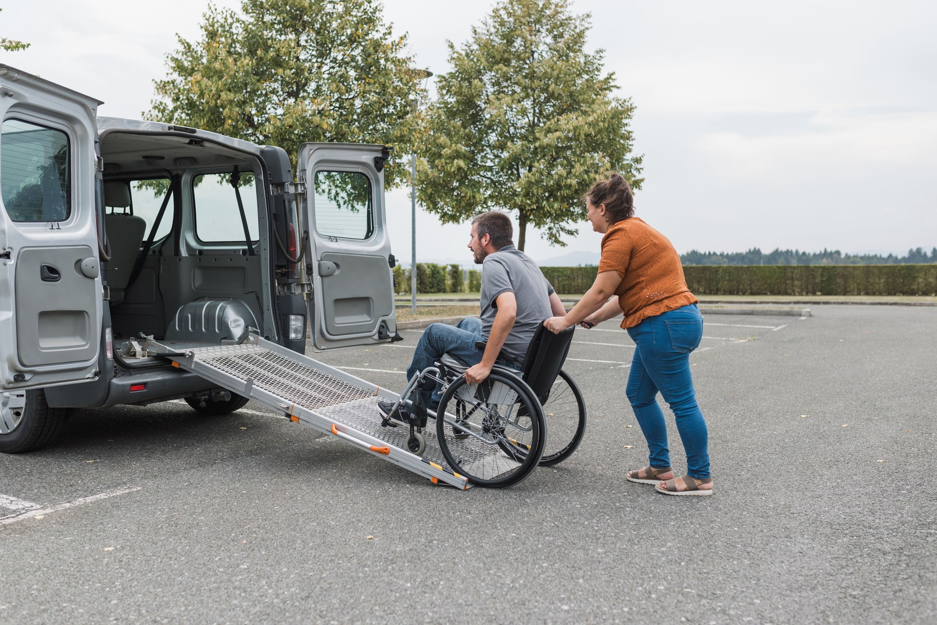 Assistant helping a person in wheelchair with transport using accessible ramp